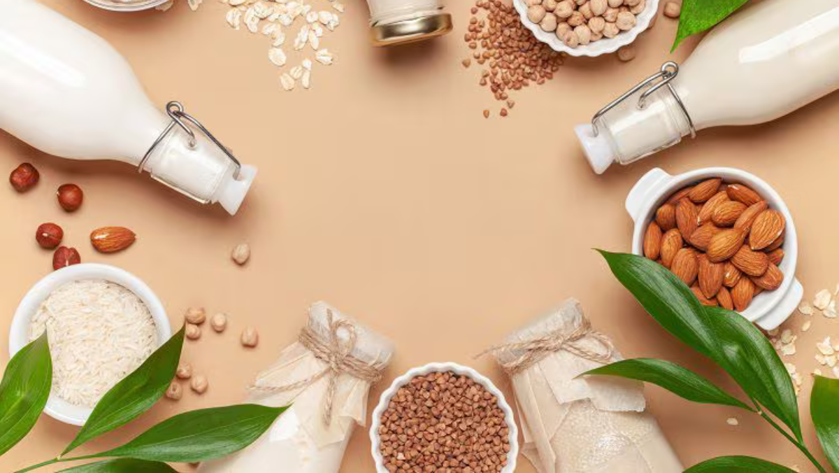 Plant-based milk bottles arranged with nuts, grains and leaves on a beige background.