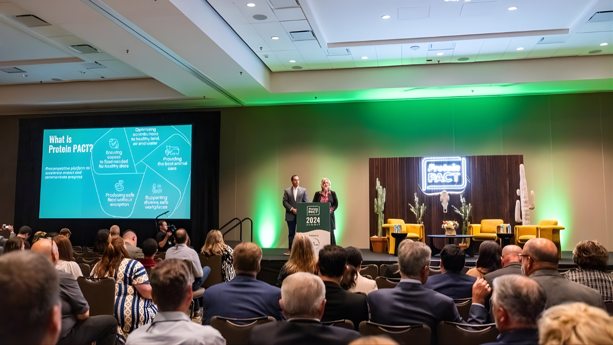 Conference audience watching Protein PACT speakers present sustainability goals on stage with bright green lighting