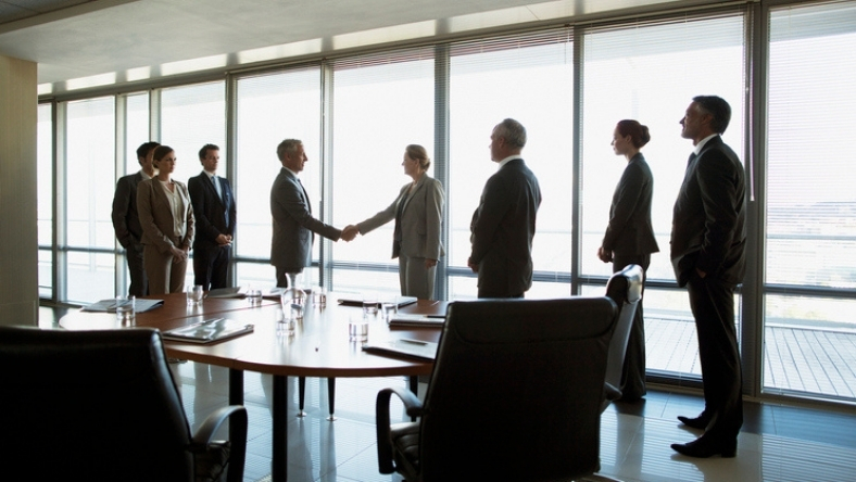 Executives shake hands during a private equity investment meeting in a corporate boardroom
