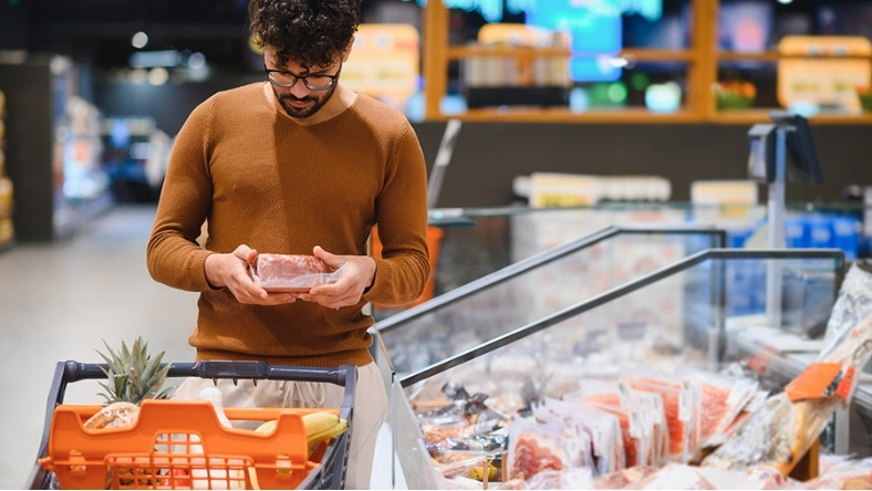 Shopper examining packaged meat products in a supermarket aisle